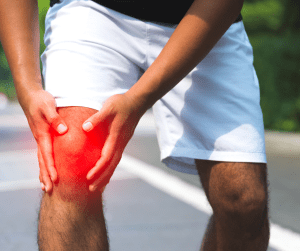 A male holding his knee because he is experiencing muscle strains. The knee is highlighted red to indicate the affected target area. 