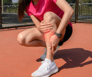 A woman holding her shin as she is experiencing shin splints. The affected shin is highlighted red to indicate the target area. 