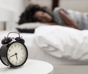 an alarm clock in the front of the image with someone sleeping blurred out in the background 